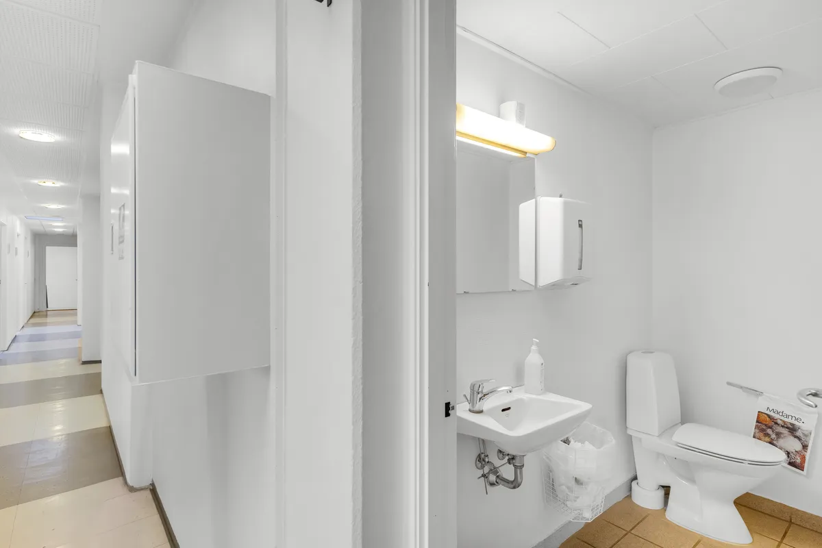 Et lille, hvidt toilet med moderne udseende, hvor toilettet og vasken er placeret ved siden af hinanden, og der er en