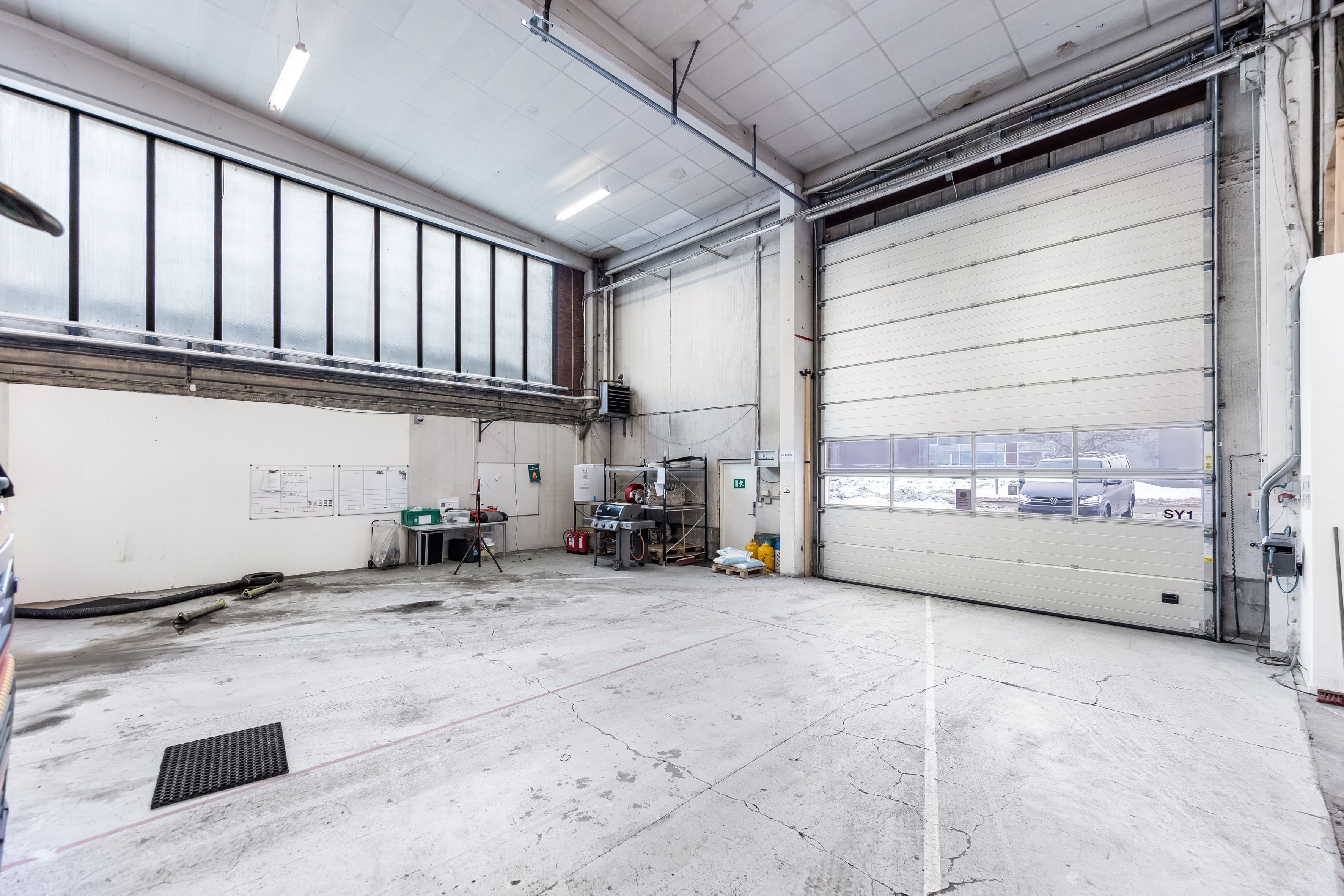 Lager med administrationslokaler og garageporte. Mange lyse og store vinduer. Forskellige værktøjer og materialer på plads.