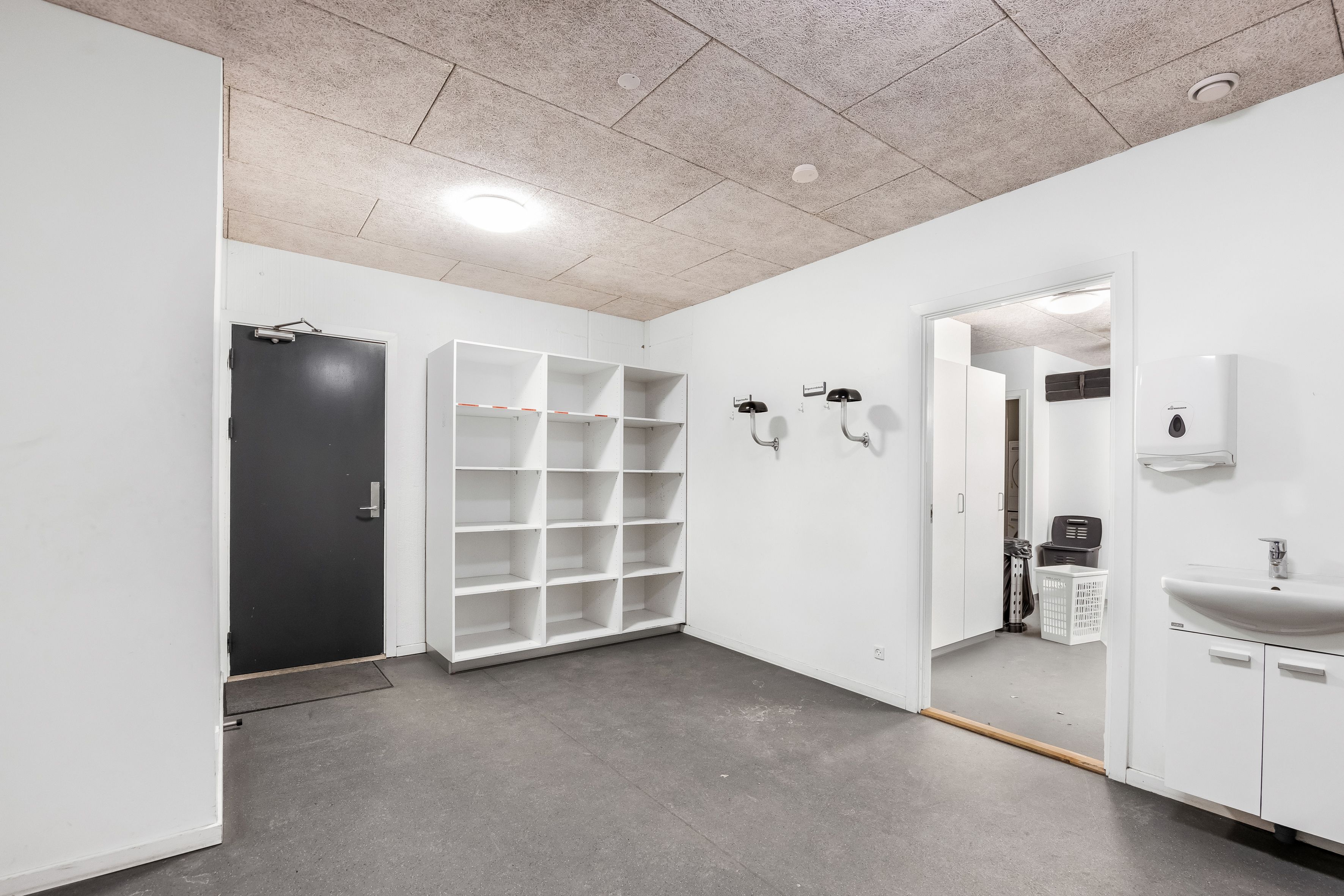 Lager med lyse lofter og moderne design. Et hvidt vægskab og en hvid håndvask med sæbeautomat. Et lukket højloftet lagerrum