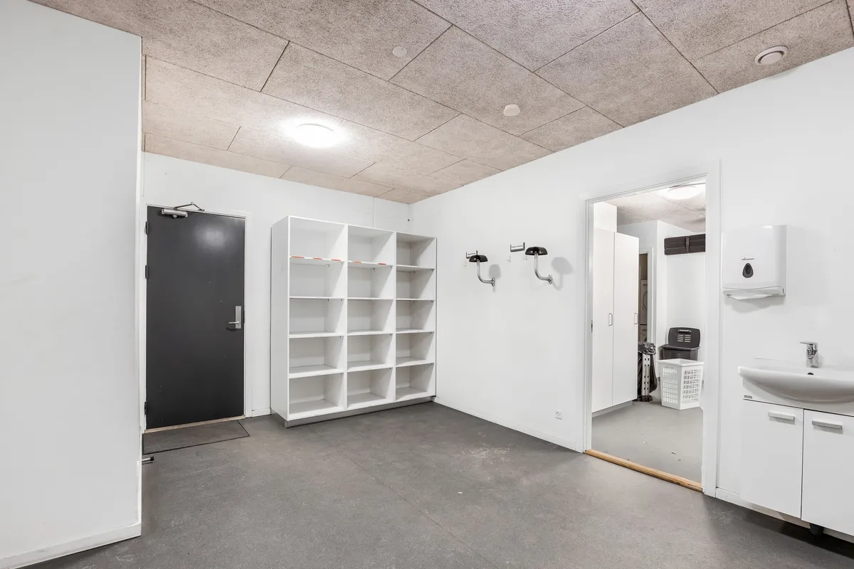 Lager med lyse lofter og moderne design. Et hvidt vægskab og en hvid håndvask med sæbeautomat. Et lukket højloftet lagerrum