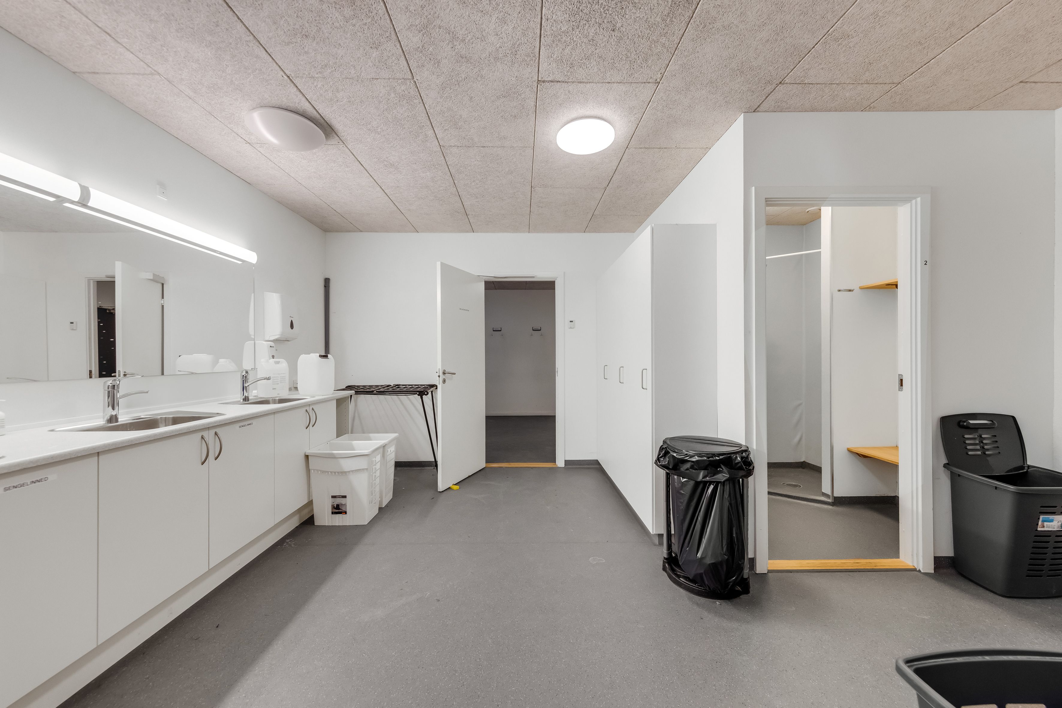 Rent og renseri lager med lyse lofter og hvide vægge, der er to åbne døre og en stor skraldspande med skraldeposer og