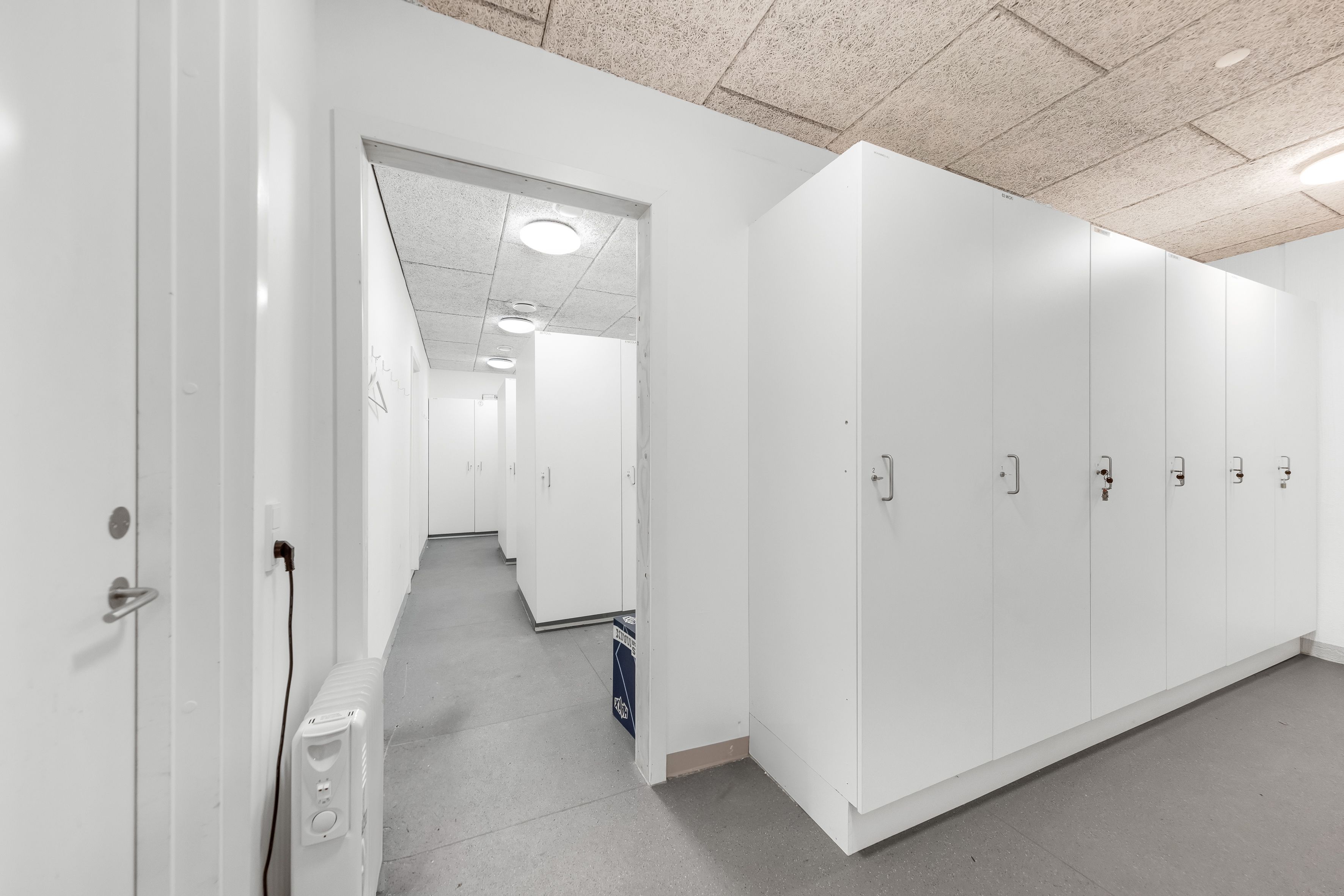 Lager med hvide vægge og loft, hvide kabiner og døre, hvidgulv og et stykke elektronisk udstyr i en hjørne.