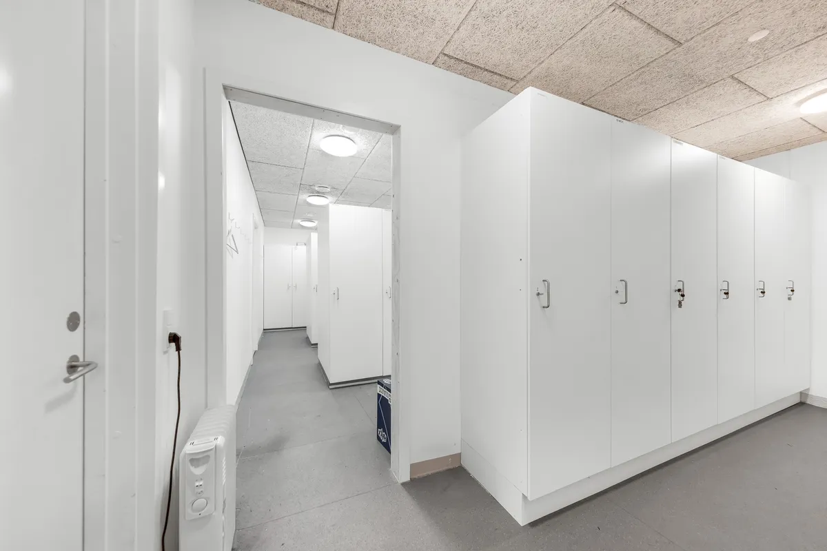 Lager med hvide vægge og loft, hvide kabiner og døre, hvidgulv og et stykke elektronisk udstyr i en hjørne.