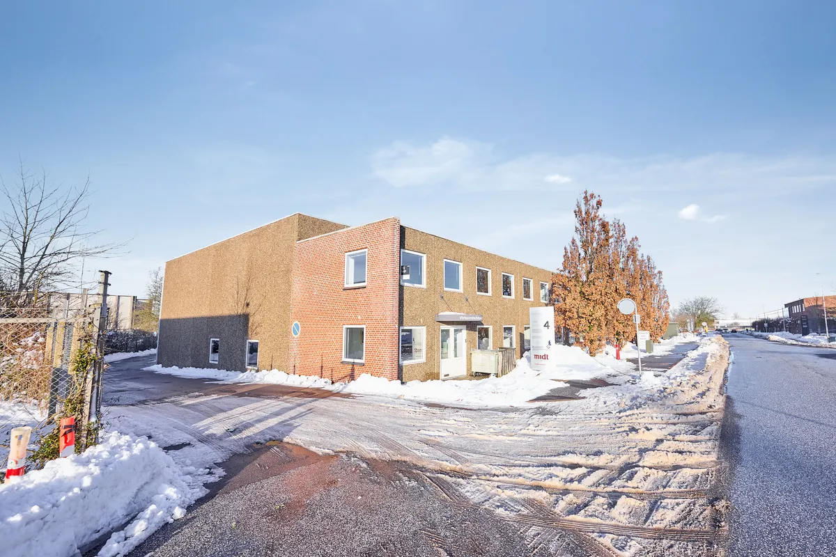 En højloftet bygning med administrationskontor og porte til lager. Bygningen er omgivet af sne, og der er en skov med træer