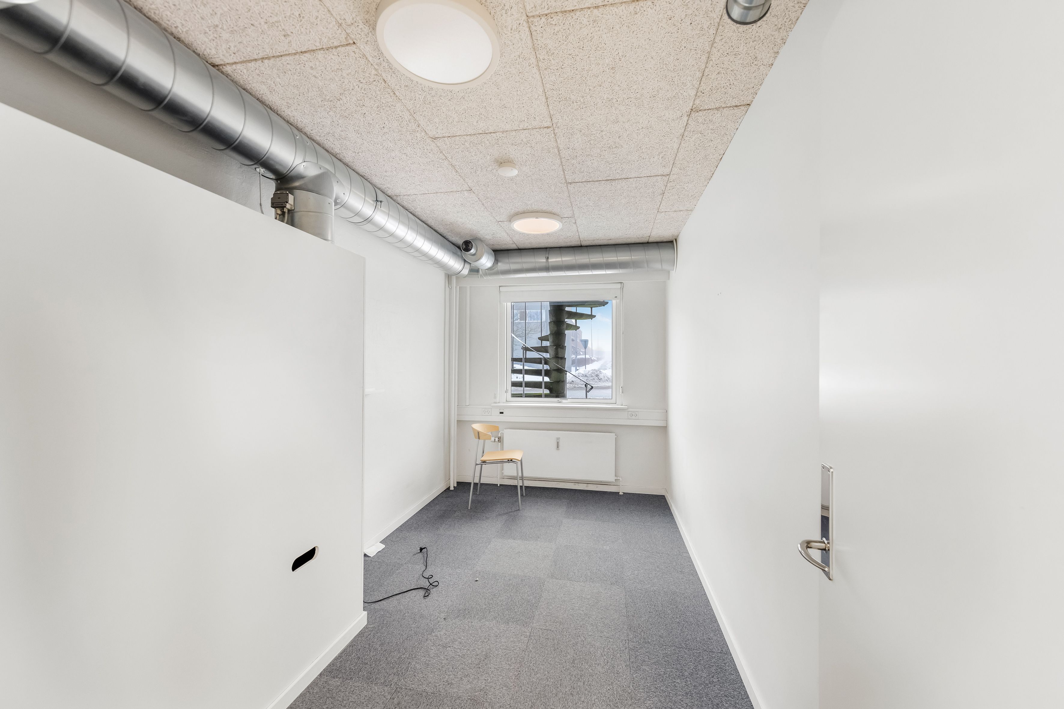 Et ubeboet lagerrum med høje hvide vægge, en lysekron, et vindue med udsigt til en stige og en stol med håndtag til at