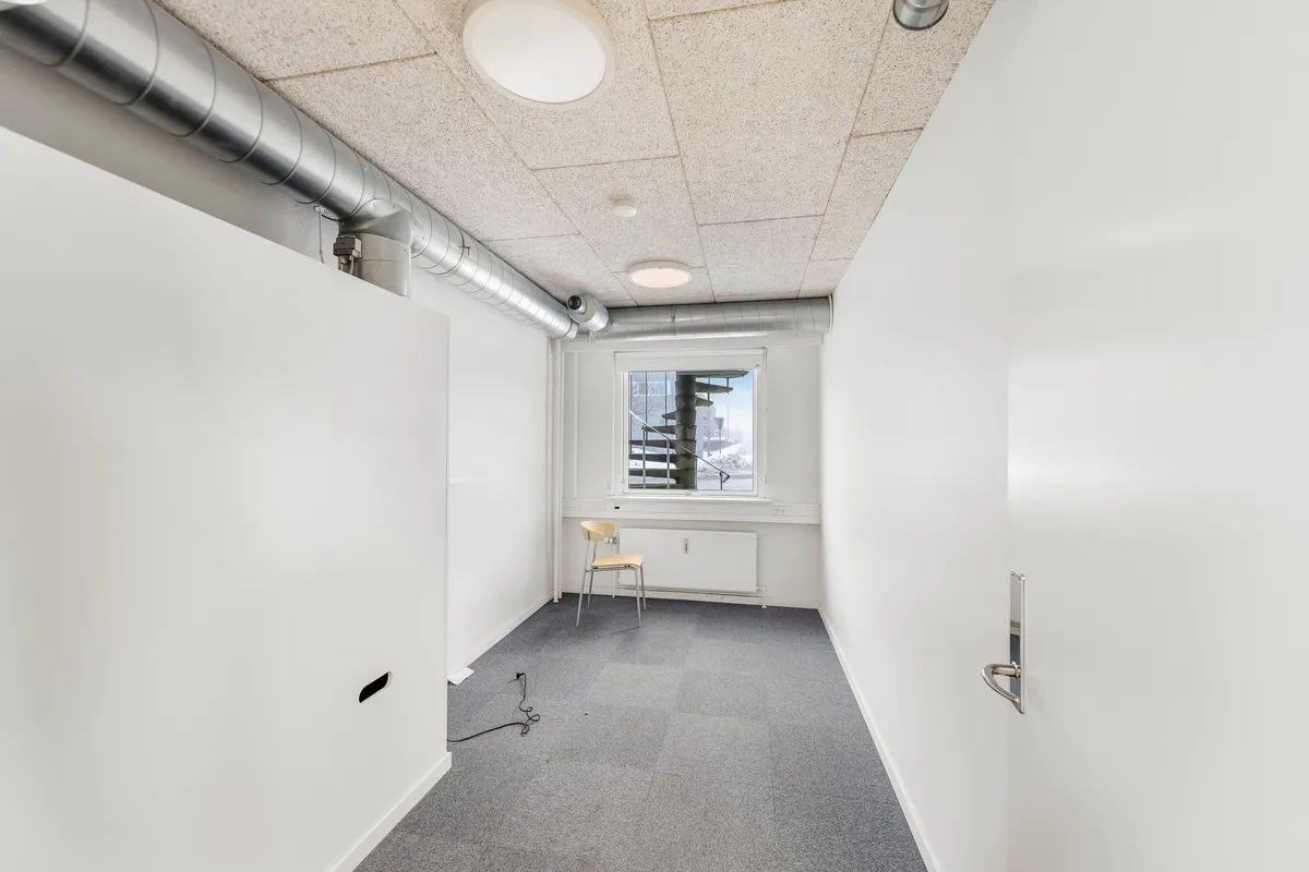 Et ubeboet lagerrum med høje hvide vægge, en lysekron, et vindue med udsigt til en stige og en stol med håndtag til at