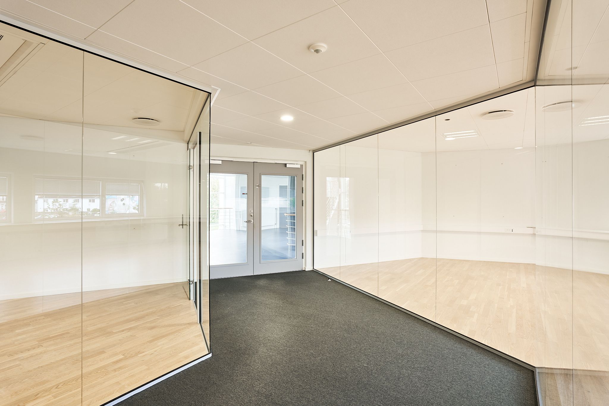 Et stort, tomt og moderne kontor med hvidt loft og gulv samt store glasvægge og en åben dør til et andet rum
