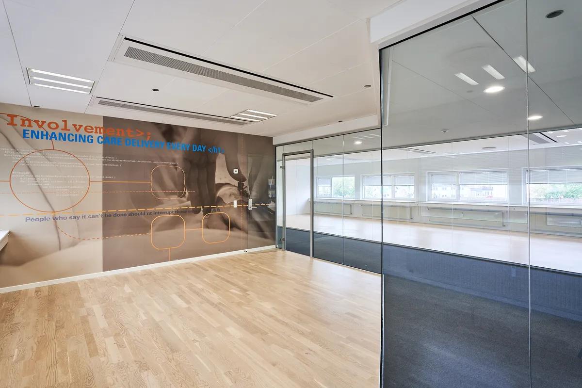 Et moderne kontor med glasvægge, hårdt trægulv og et stort vægmaleri med tekst og billeder