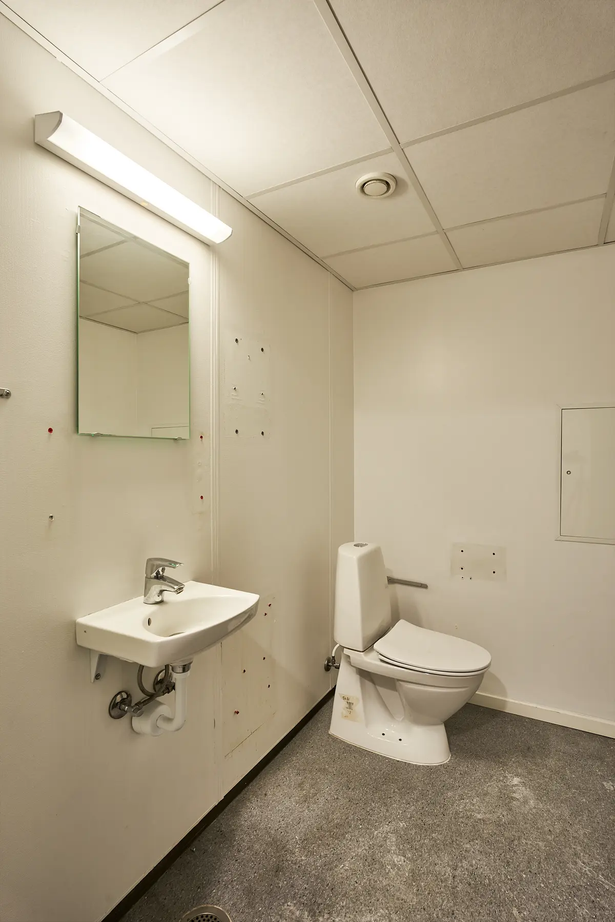 Et lille, hvidmalet toilet med moderne udstyr, et højt monteret spejl og et rent gulv