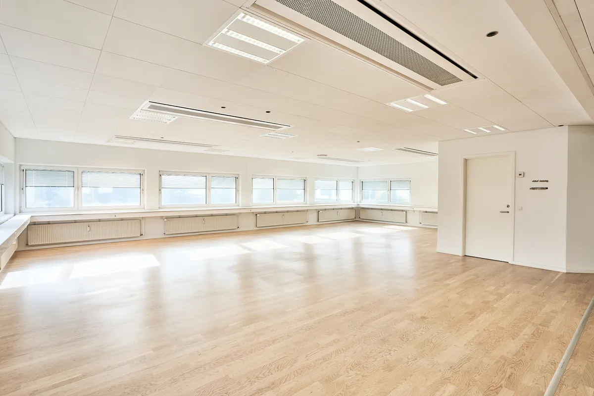 Rummelig lokale med højt loft, hvidmaling, lyse trægulve og store vinduer med gardiner for at give meget naturligt lys