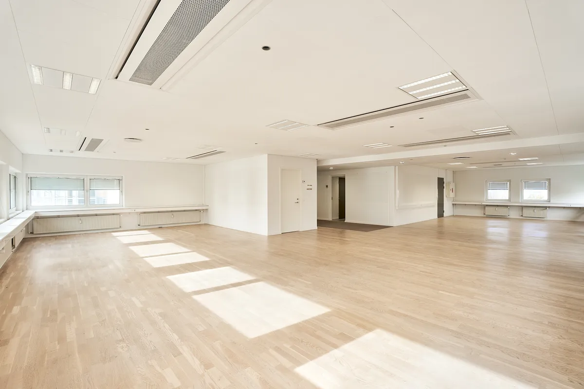 Et stort, tomt lokale med lyse trægulve og hvide vægge, lyse vinduer og lysepunkter på loftet