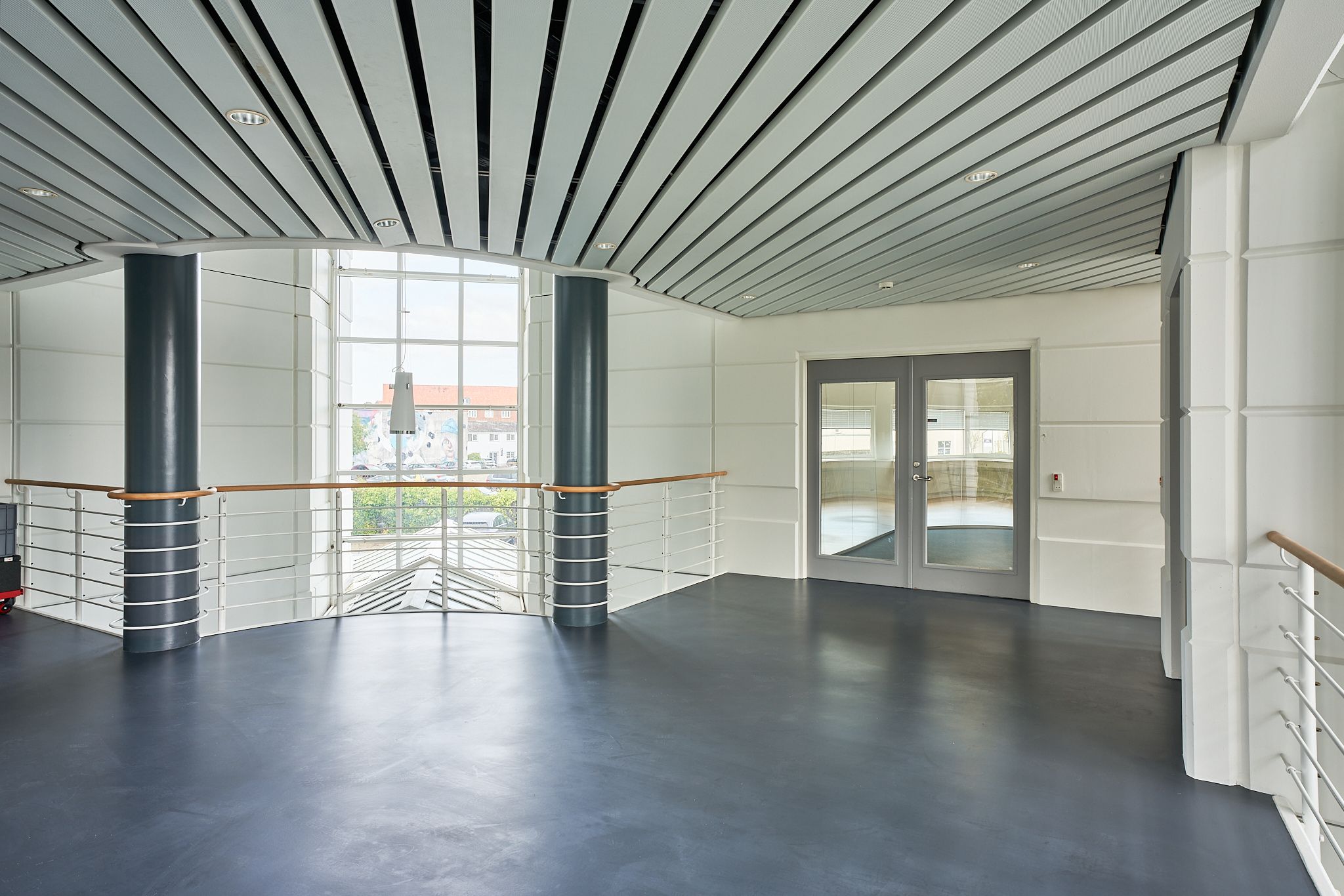 Hvidmalet atrium med slanke søjler og glasvinduer giver en åben og moderne atmosfære. Store, lyse vinduespartier og