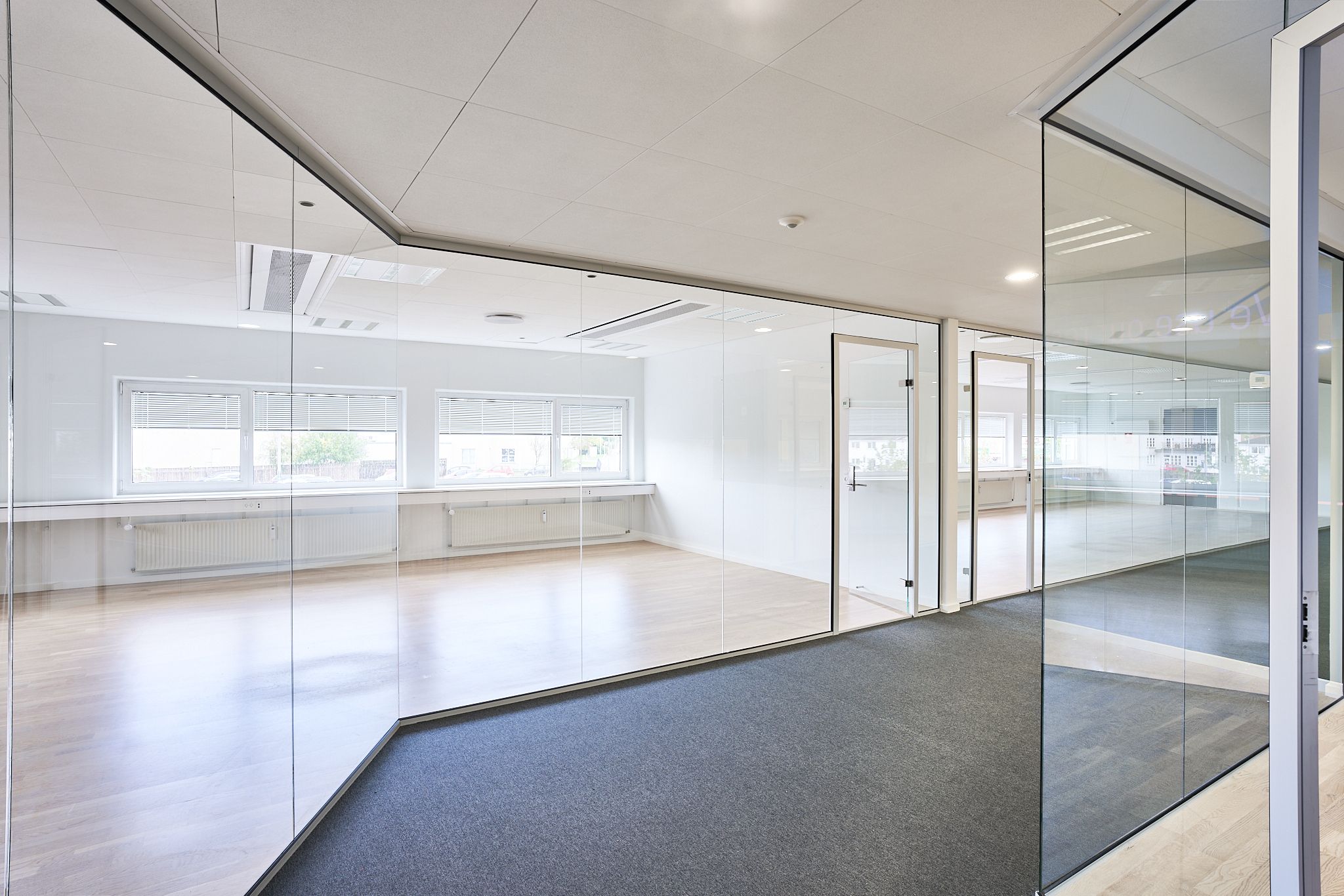 Moderne kontor med hvide vægge, glaspaneler og trægulv. Aircondition enheder og radiatorer langs væggen. Vinduespartier med