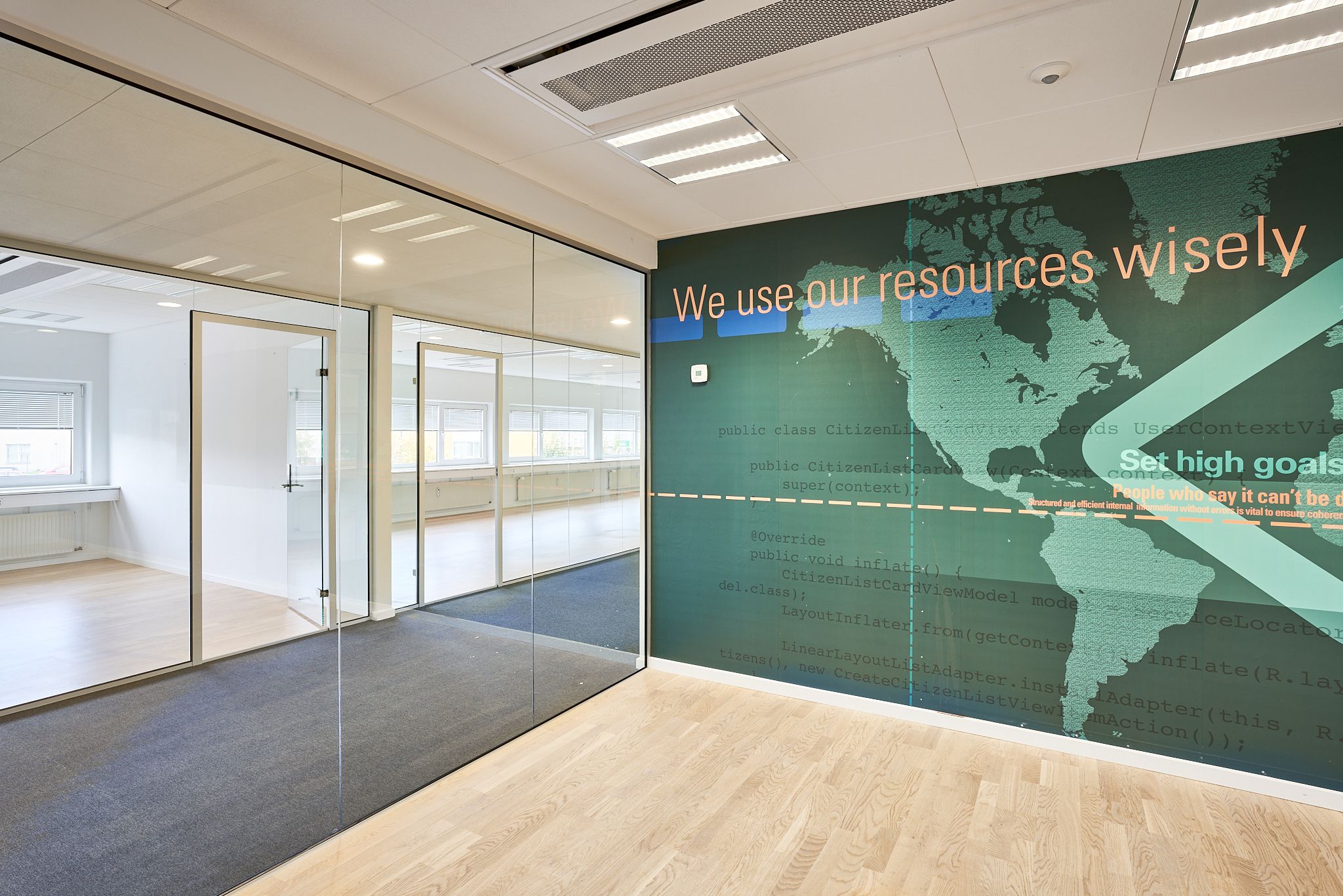Kontorrum med to glasdøre og en stor væg med citatet: We use our resources wisely.