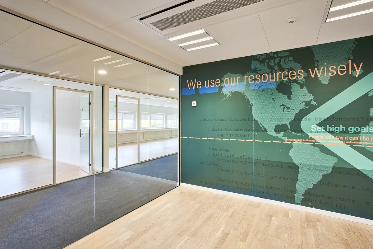 Kontorrum med to glasdøre og en stor væg med citatet: We use our resources wisely.