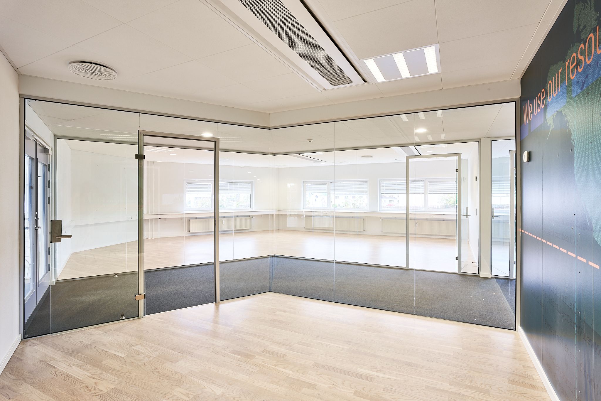 En stor, tom konferencesal med hvide vægge, glasdøre og gulve. Værelset er lyst og moderne med hvide lofter og store vinduer.