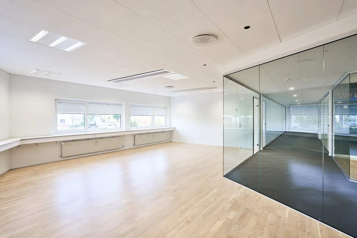 En moderne kontorbygning med hvide vægge, trægulv og store glasruder med gardiner. Der er luftkøleapparater under