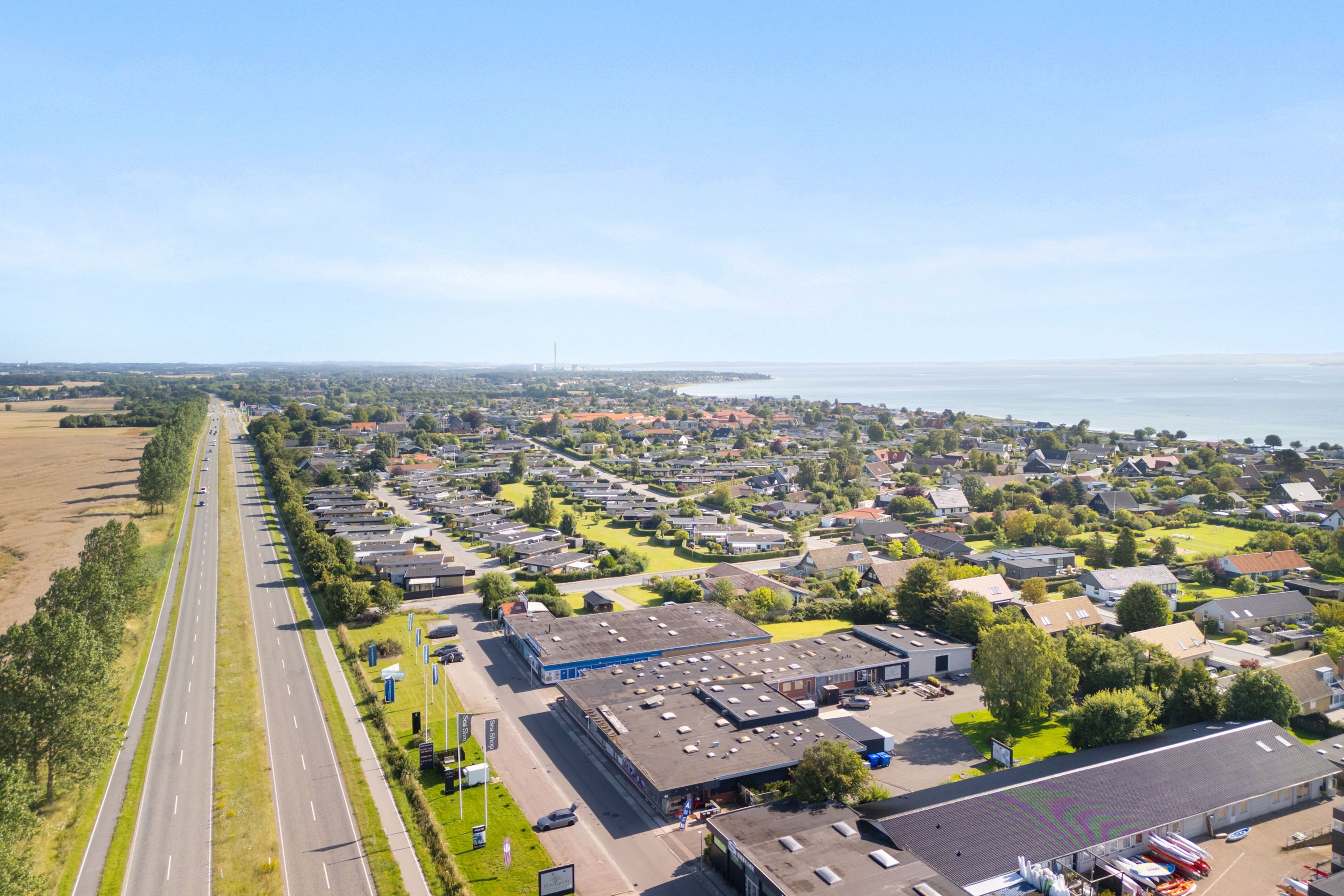 Flyfoto af landsby med vej, bygninger og hav på baggrunden, med skov og parker mellem bygningerne