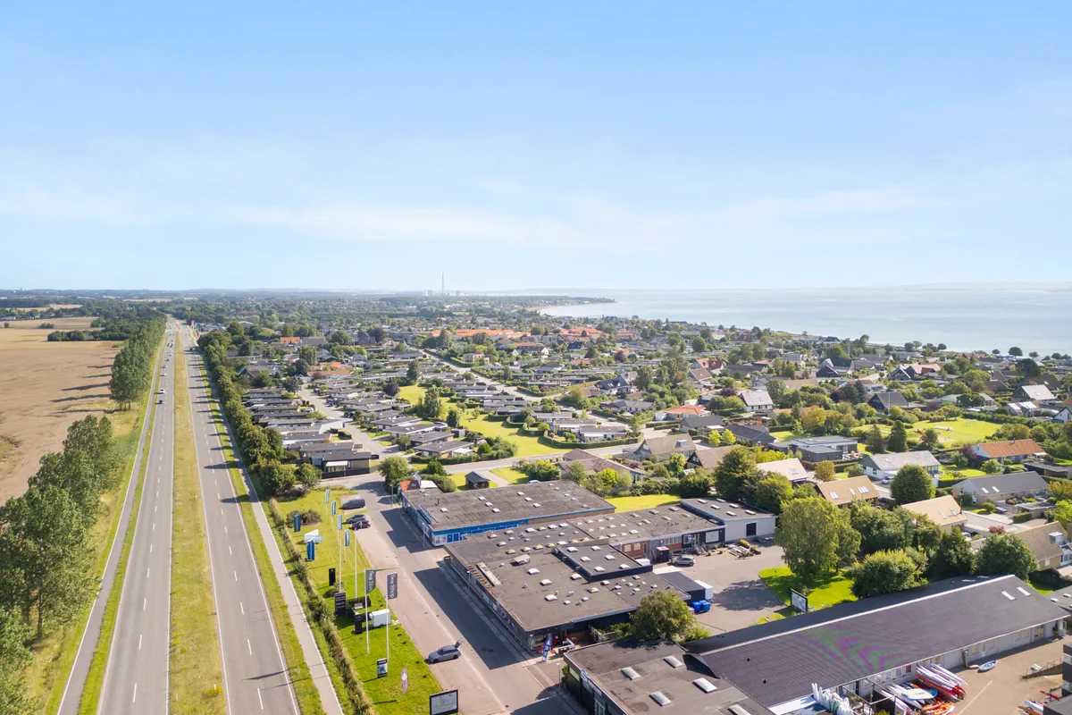 Flyfoto af landsby med vej, bygninger og hav på baggrunden, med skov og parker mellem bygningerne