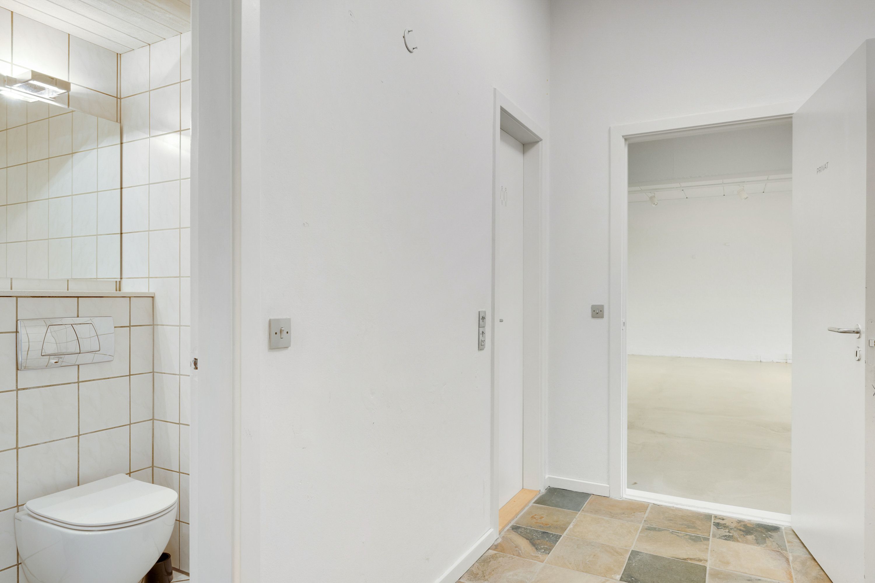 Lejlighed med moderne, hvidt badeværelse og åbent værelse med skifergulv, der giver mulighed for showroom eller kontorlokaler