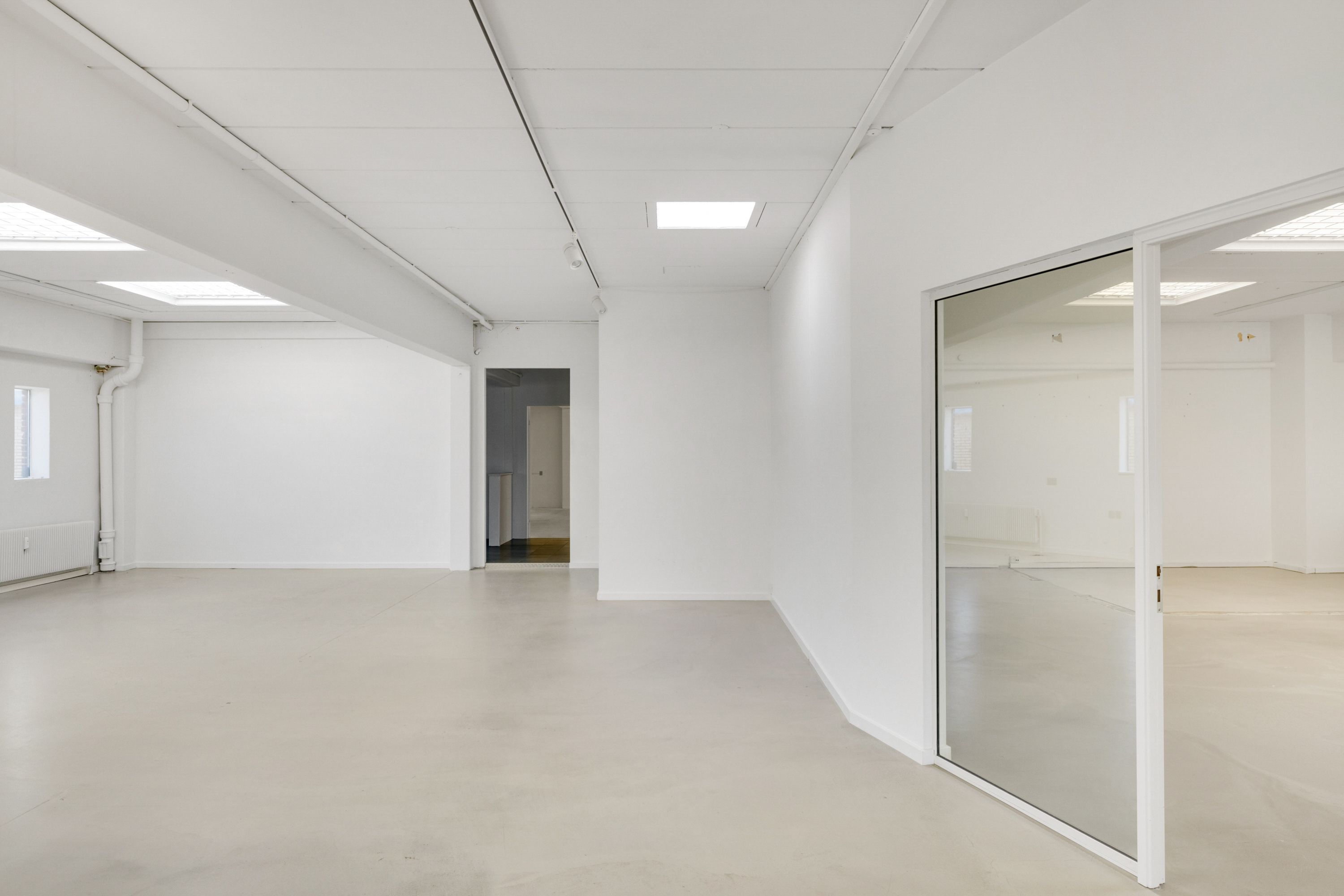 En stor, ubenyttet og hvidmalet lokale med glasdøre, lys og et åbent rum i baggrunden