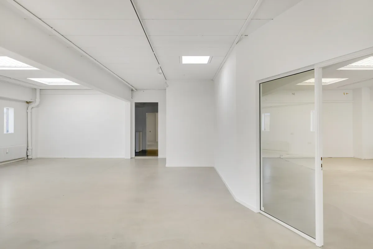 En stor, ubenyttet og hvidmalet lokale med glasdøre, lys og et åbent rum i baggrunden