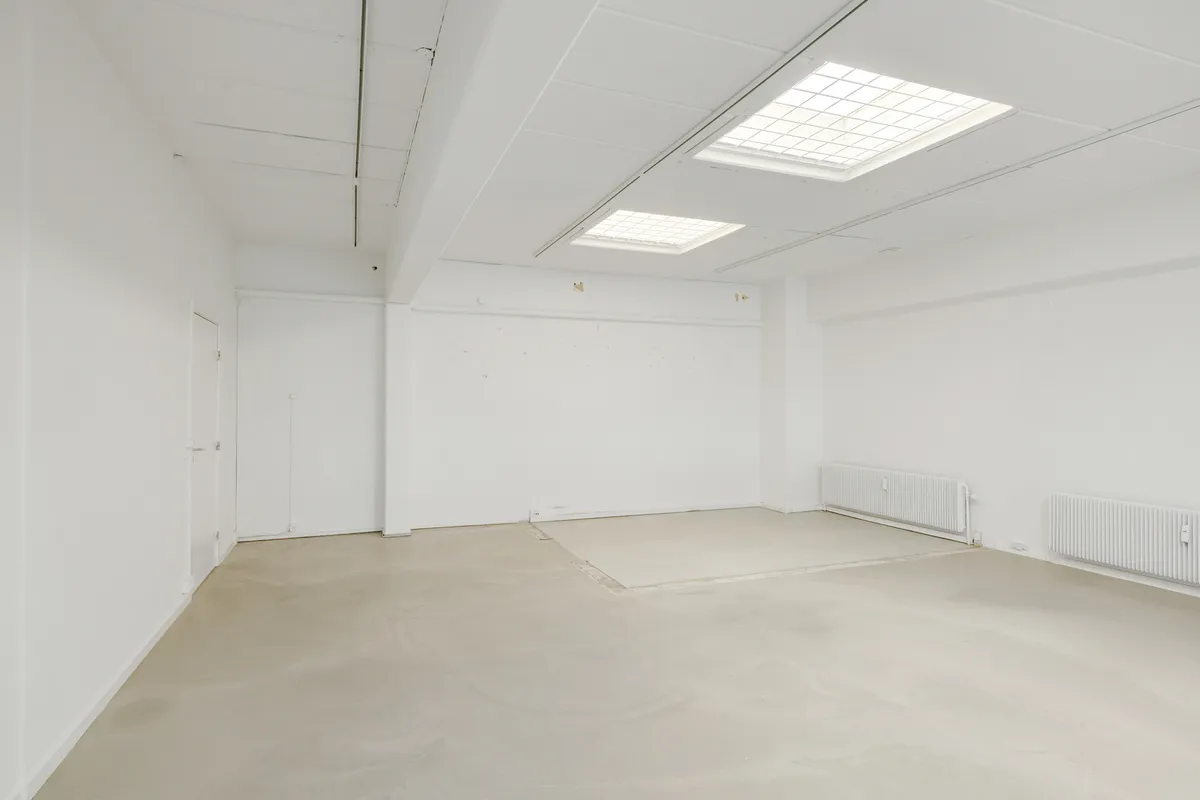 Lokaler med hvidt loft og vægge samt to radiatorer til højre samt to vinduer til loftet og to døre på den ene side