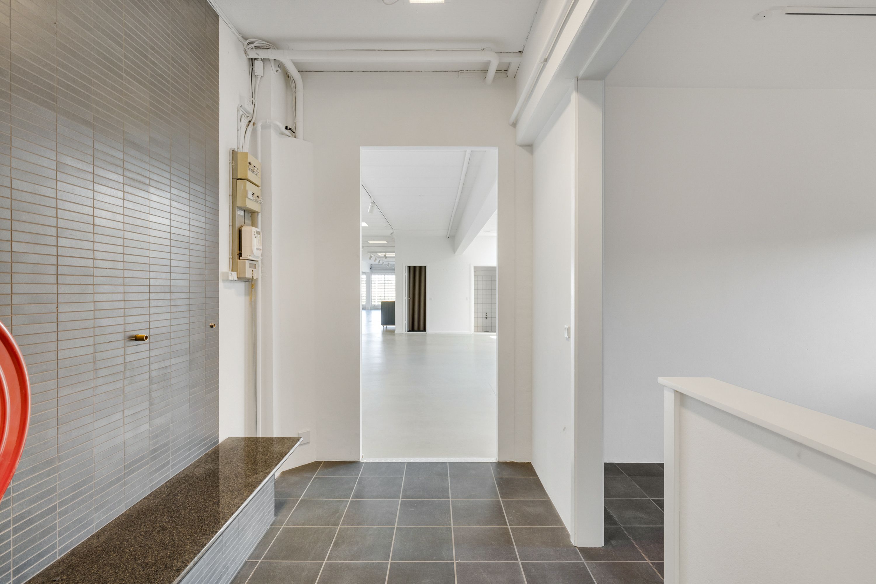 Indenfor et minimalistisk lokale med hvide vægge og gulve er der en række kakelægning og en lille bank med granitforside