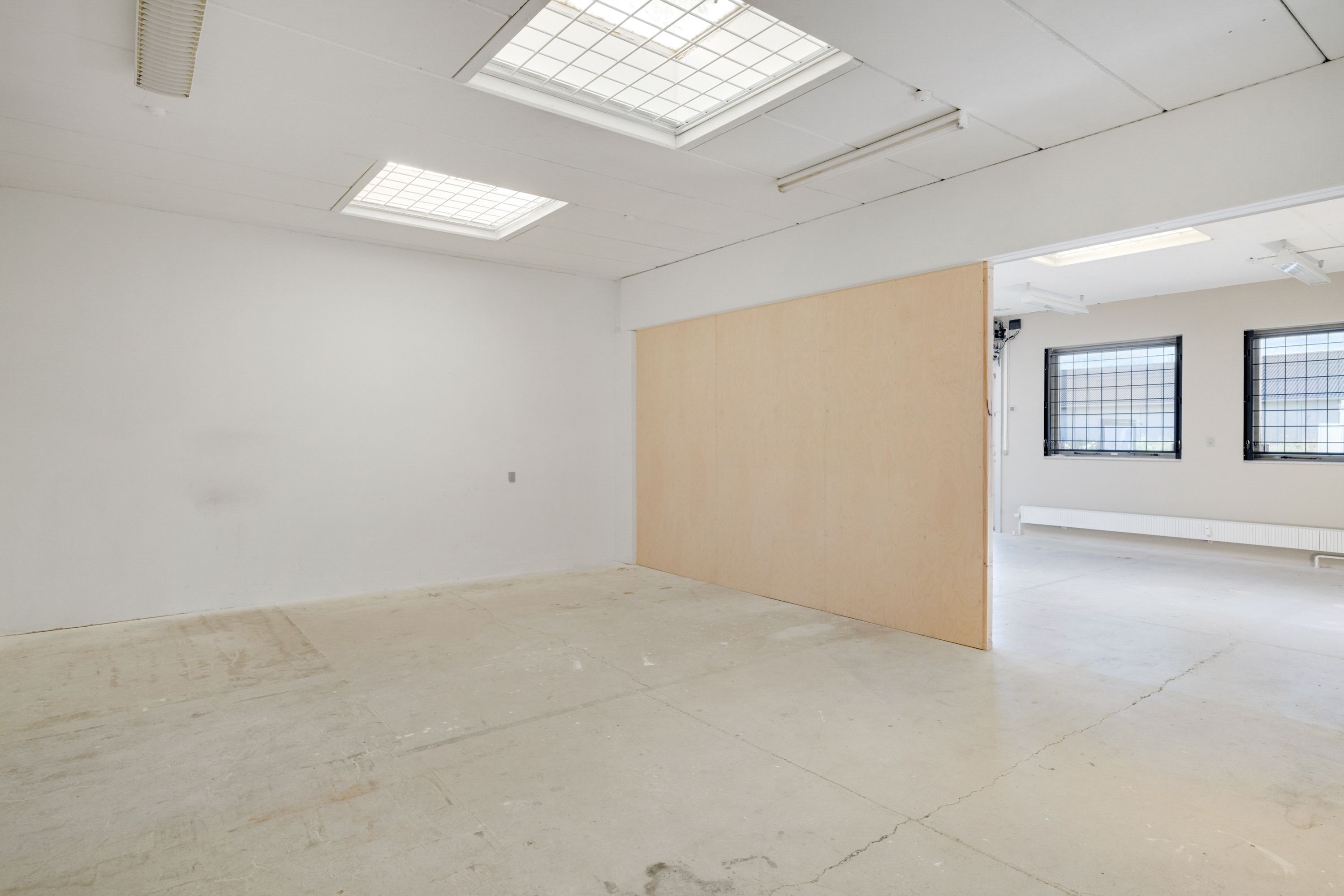 En stor og ren mødelokale med hvide vægge, lyse loftsvinduer og lyse indbyggede lys.