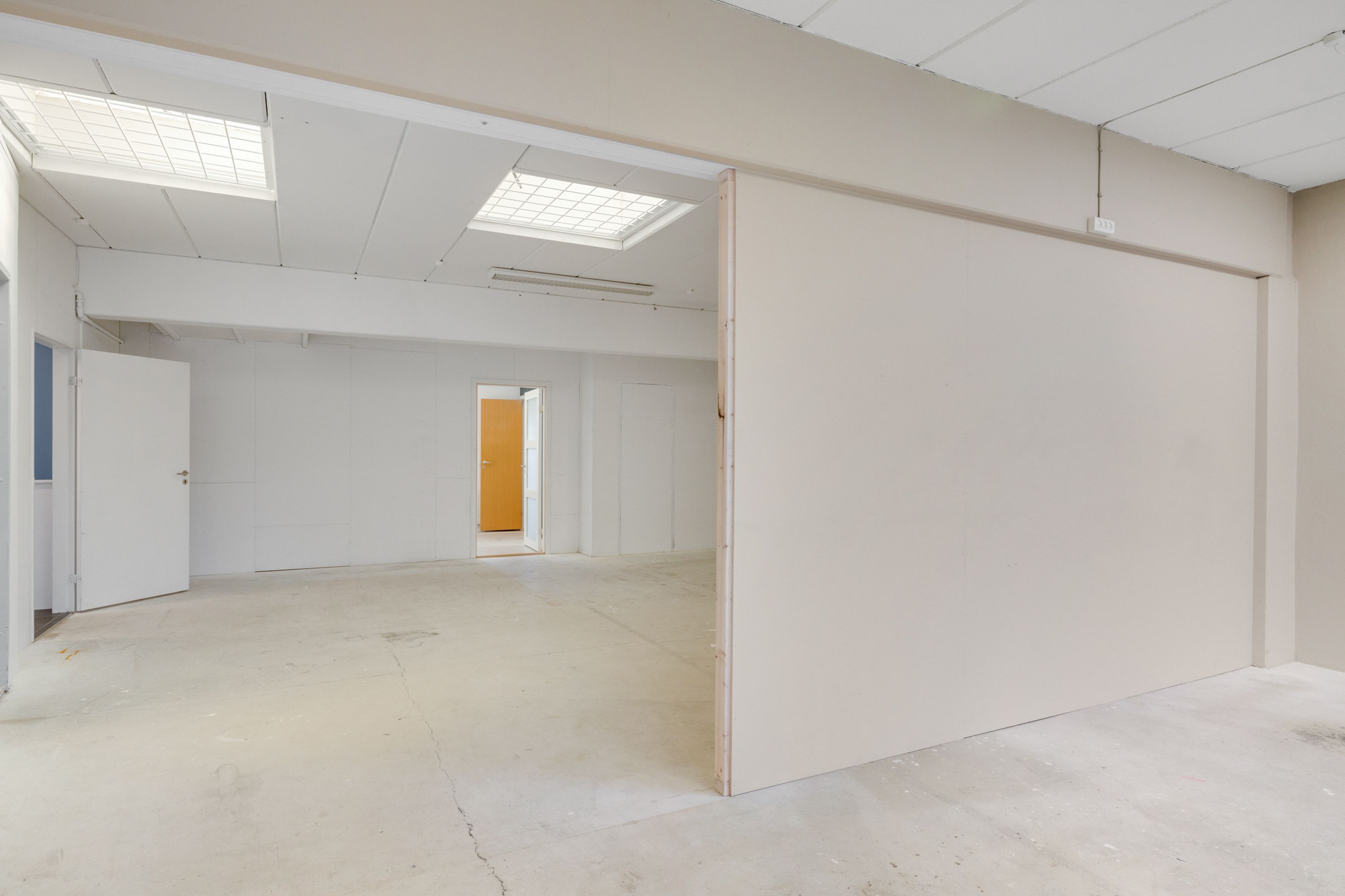 Rummelig og lys industrilokale med hvide vægge og lofter, to indgange og en åben dør mod udgangen