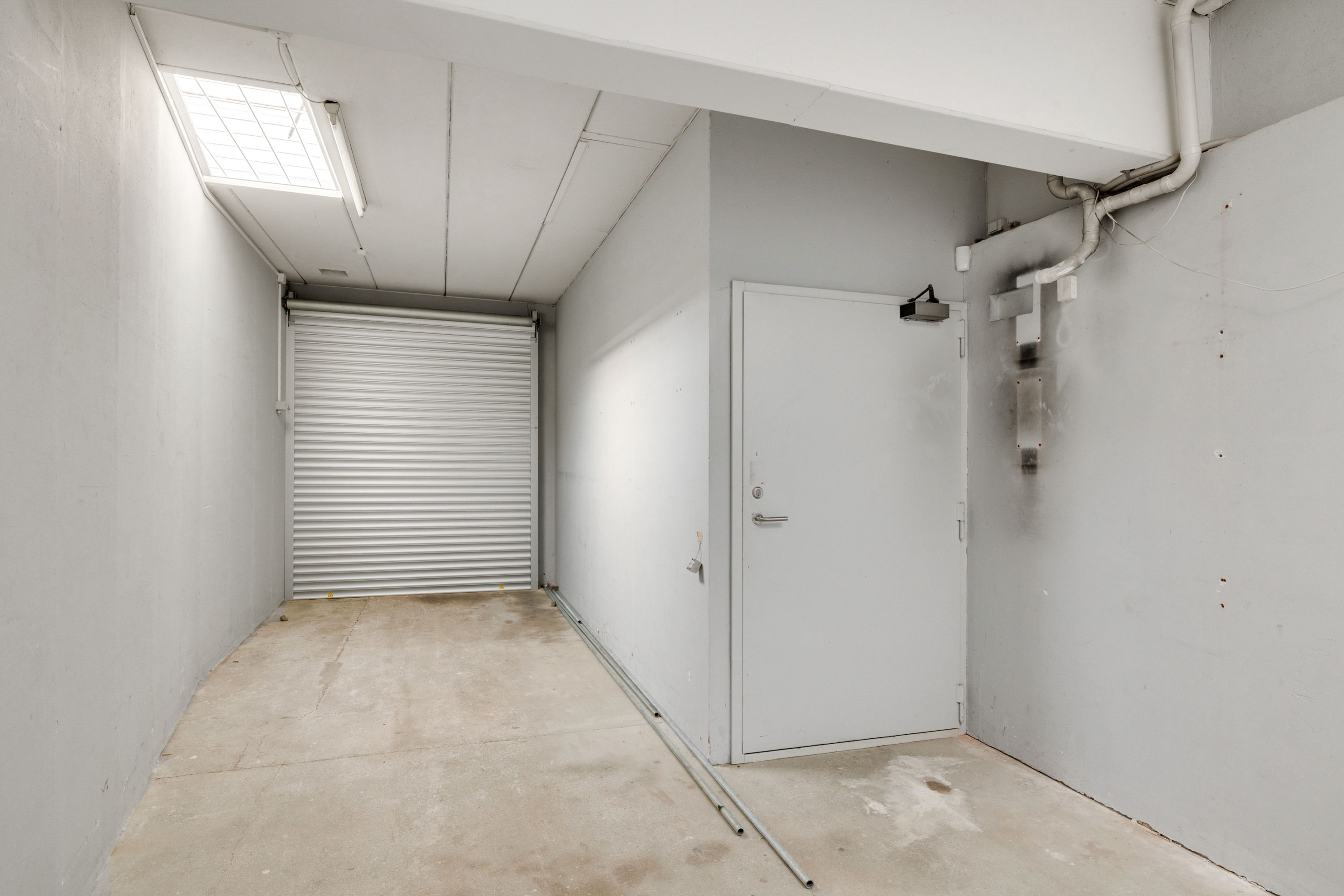 Lejlighed med garagedør og hvide vægge med lyse strimler, to døre, og elektriske ledninger.