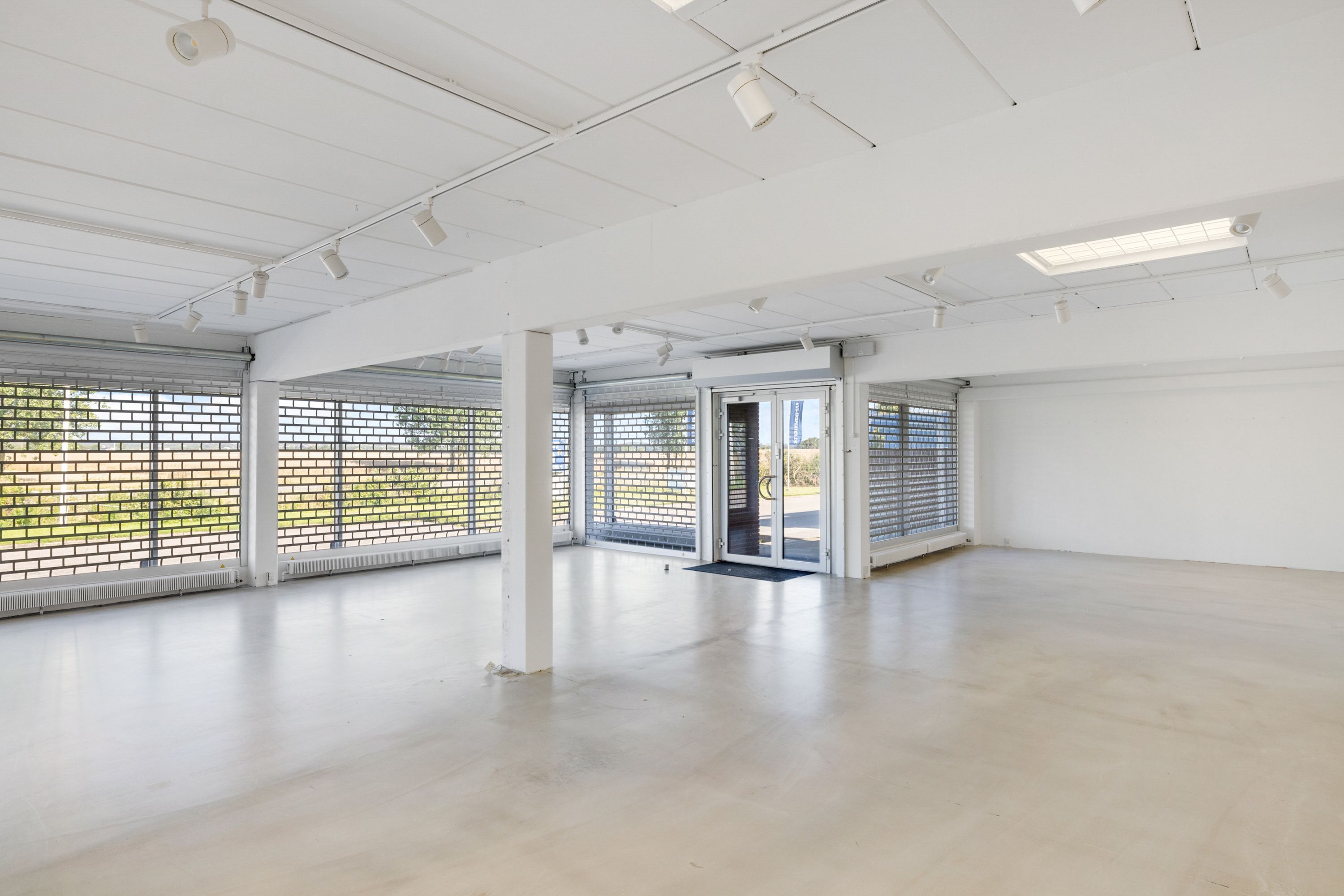 Store, moderne lokaler med hvide vægge, lysekroner og store ruder til showroom med kontor. Lokalerne er pænt og rummelige