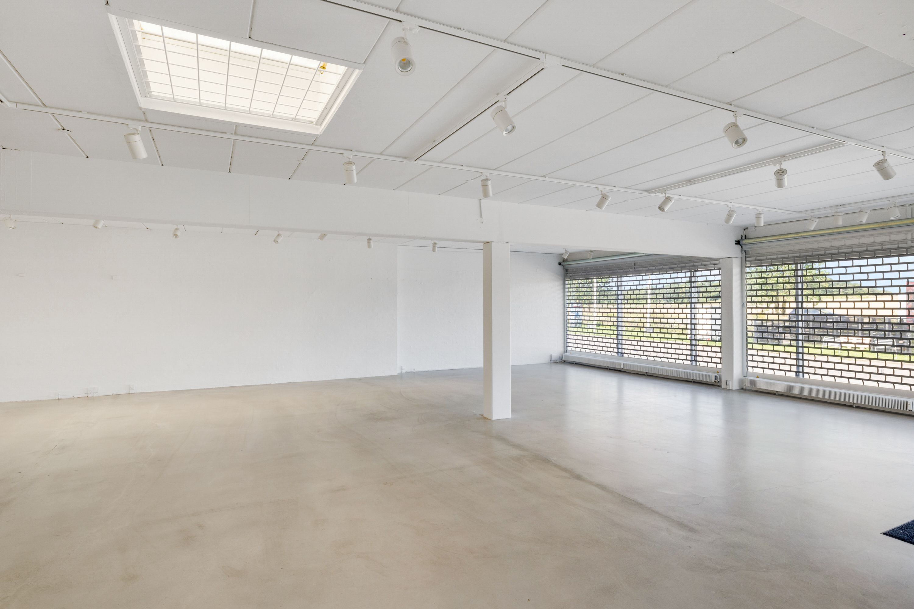 Tomt lokale med hvidt loft og gulv, udstyret med moderne lysekroner og ventiler samt udsigt til udenfor