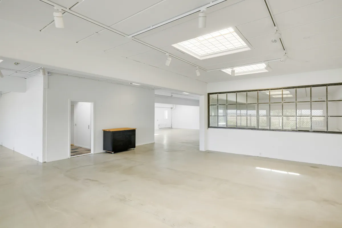 Store lokaler med højloft, lys og lysevinduer og hvid maling på væggene. En høj, sort og brun skab med hjul står i rummet.