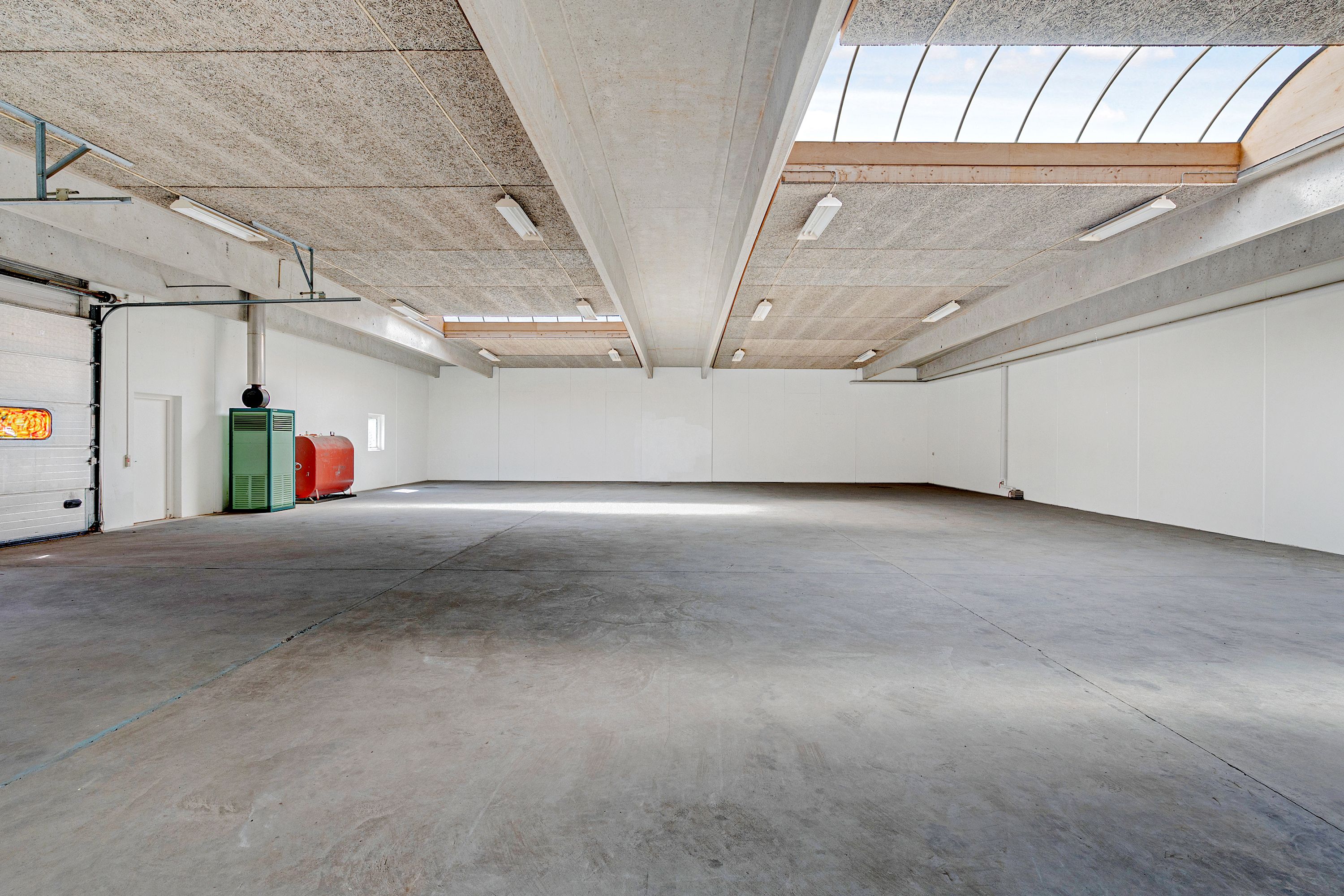 Tom garage i et erhvervspark med hvide vægge, højloft, store vinduer og cementgulv samt forskellige udstyr i nærheden