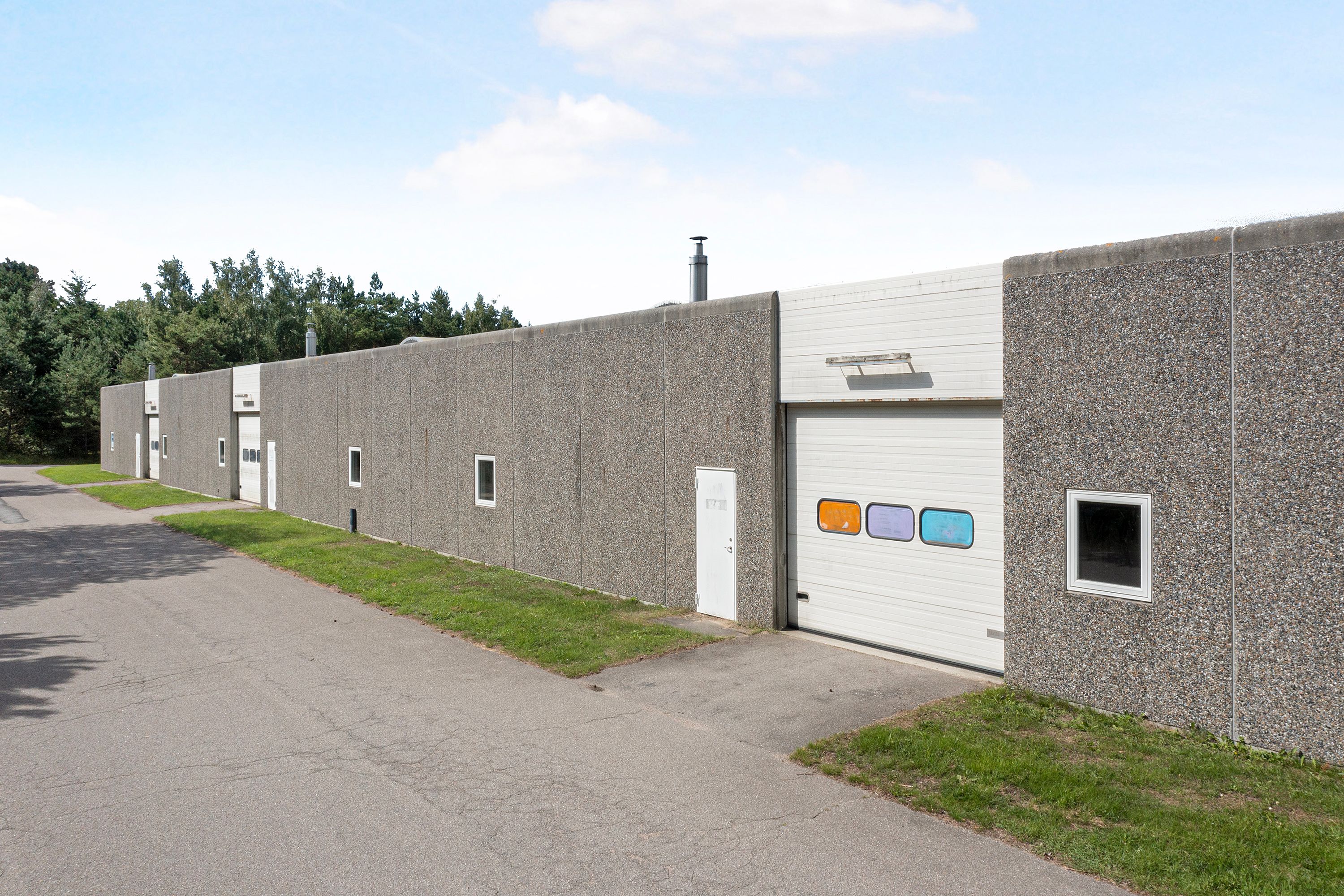 En stor erhvervsbygning med mange garageporte og vinduer og en grøn vej foran