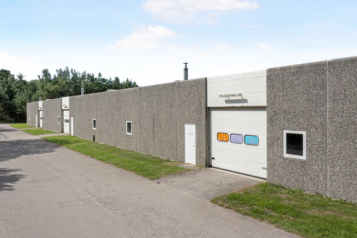 En stor erhvervsbygning med mange garageporte og vinduer og en grøn vej foran