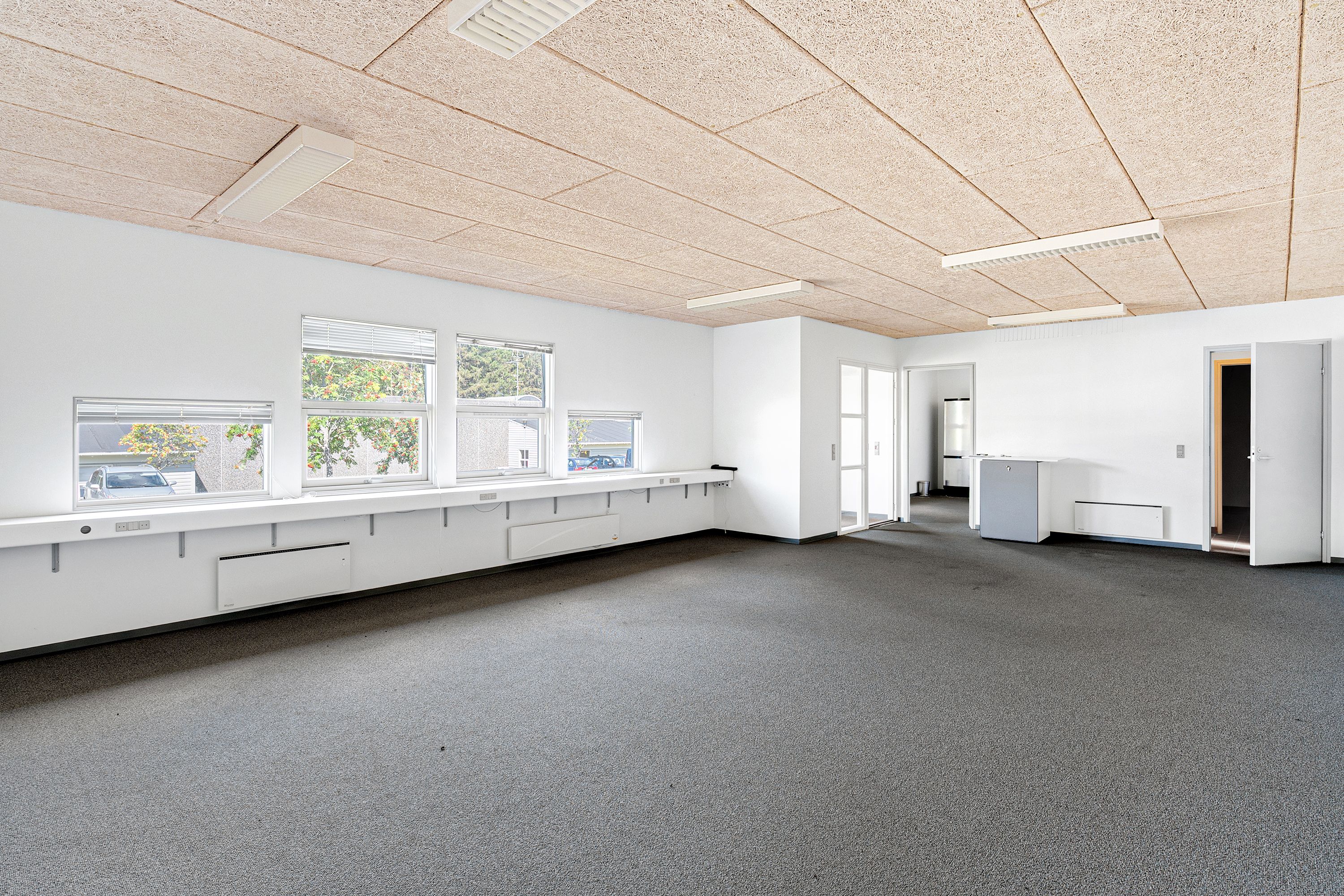 En stor, lukket, lys og møbleret lokale med karpet og vinduer, to åbne døre og en lukket dør til en mindre sidelokal