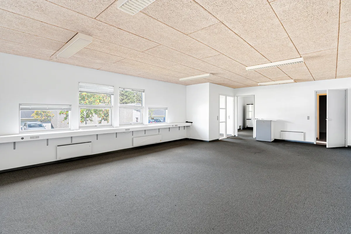 En stor, lukket, lys og møbleret lokale med karpet og vinduer, to åbne døre og en lukket dør til en mindre sidelokal