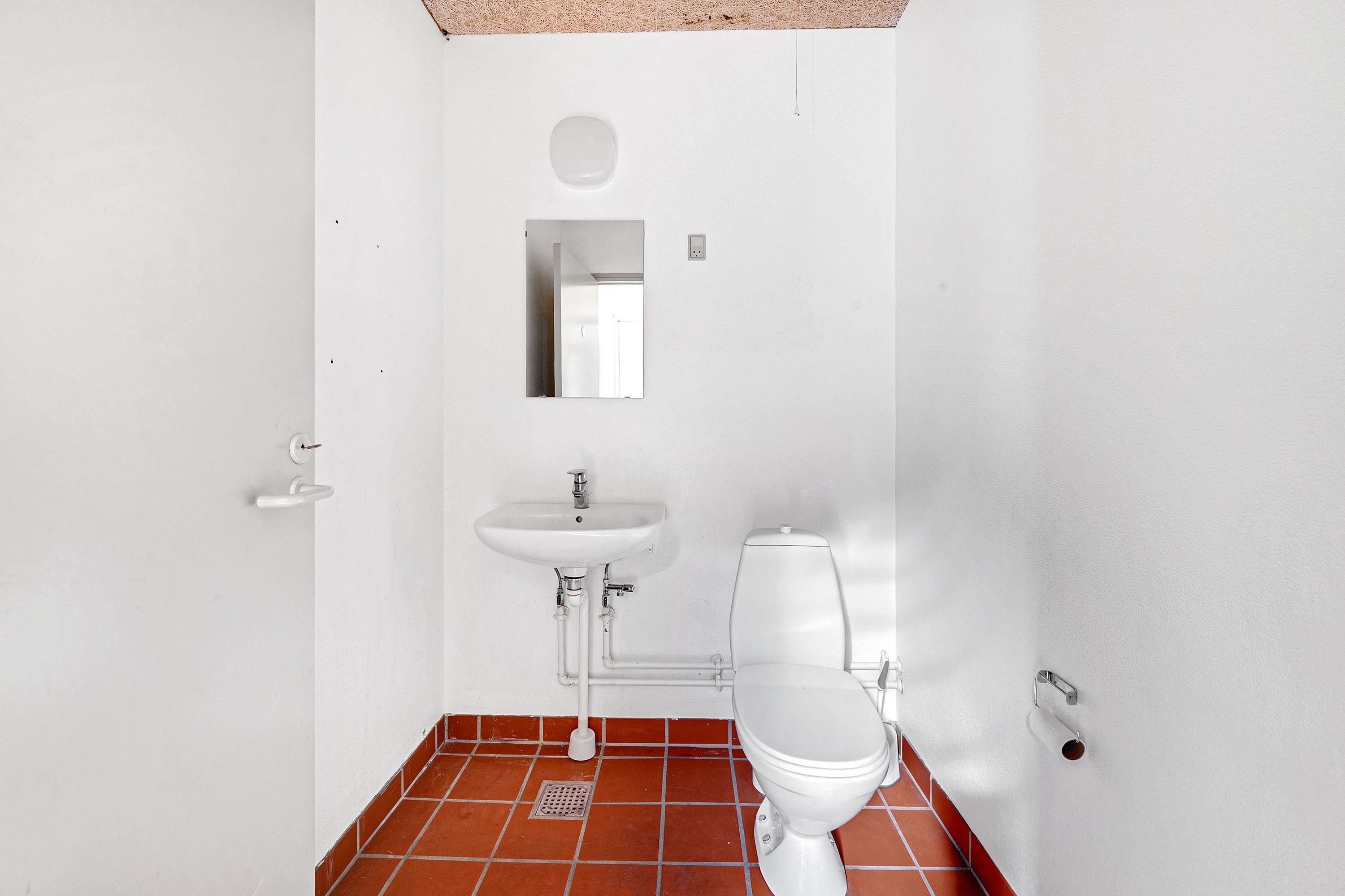 Et lille, rent og rent toilet med et hvidt toilet, en hvid vask med vandhane og et håndklædehylde på den ene side og et