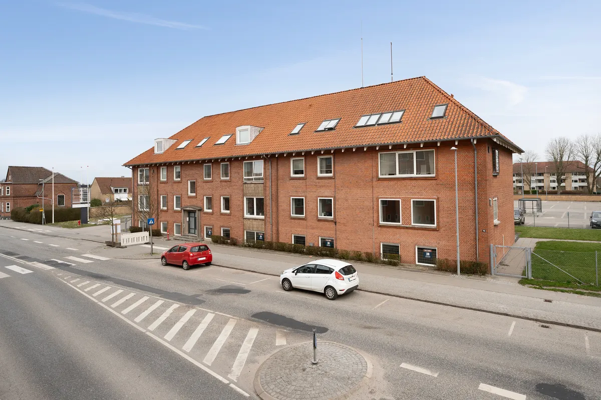 Et lejlighedshus med røde mursten og vinduer med hvide indramninger, og to biler parkeret foran