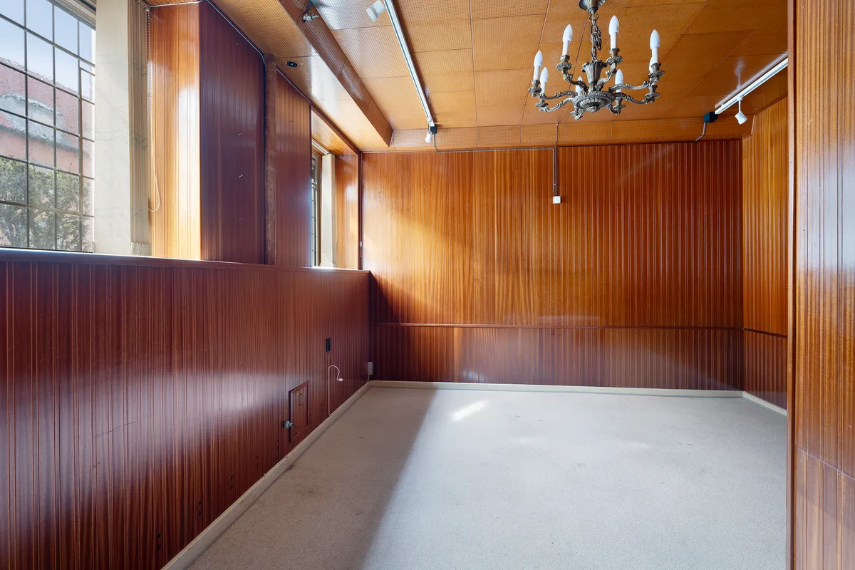 Store kælderlejemål med lyse, træpanelerede vægge og højt til loftet samt lysekroner og et vindue med en udsigt til en grøn