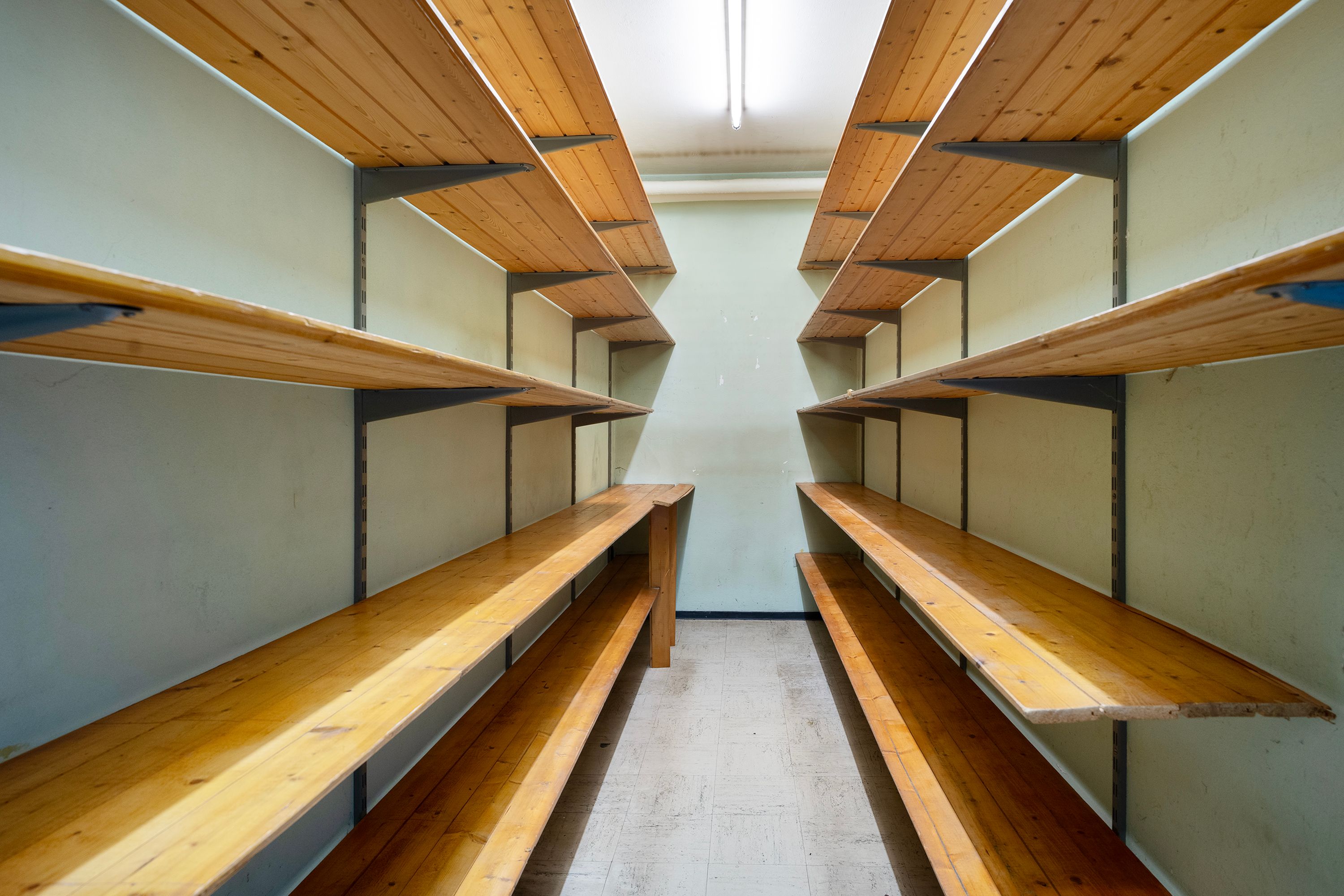 To lange, høje, lyse træhylder med firkantede bærebrætter, der er ophængt på en hvid væg med firkantede stålbøjler