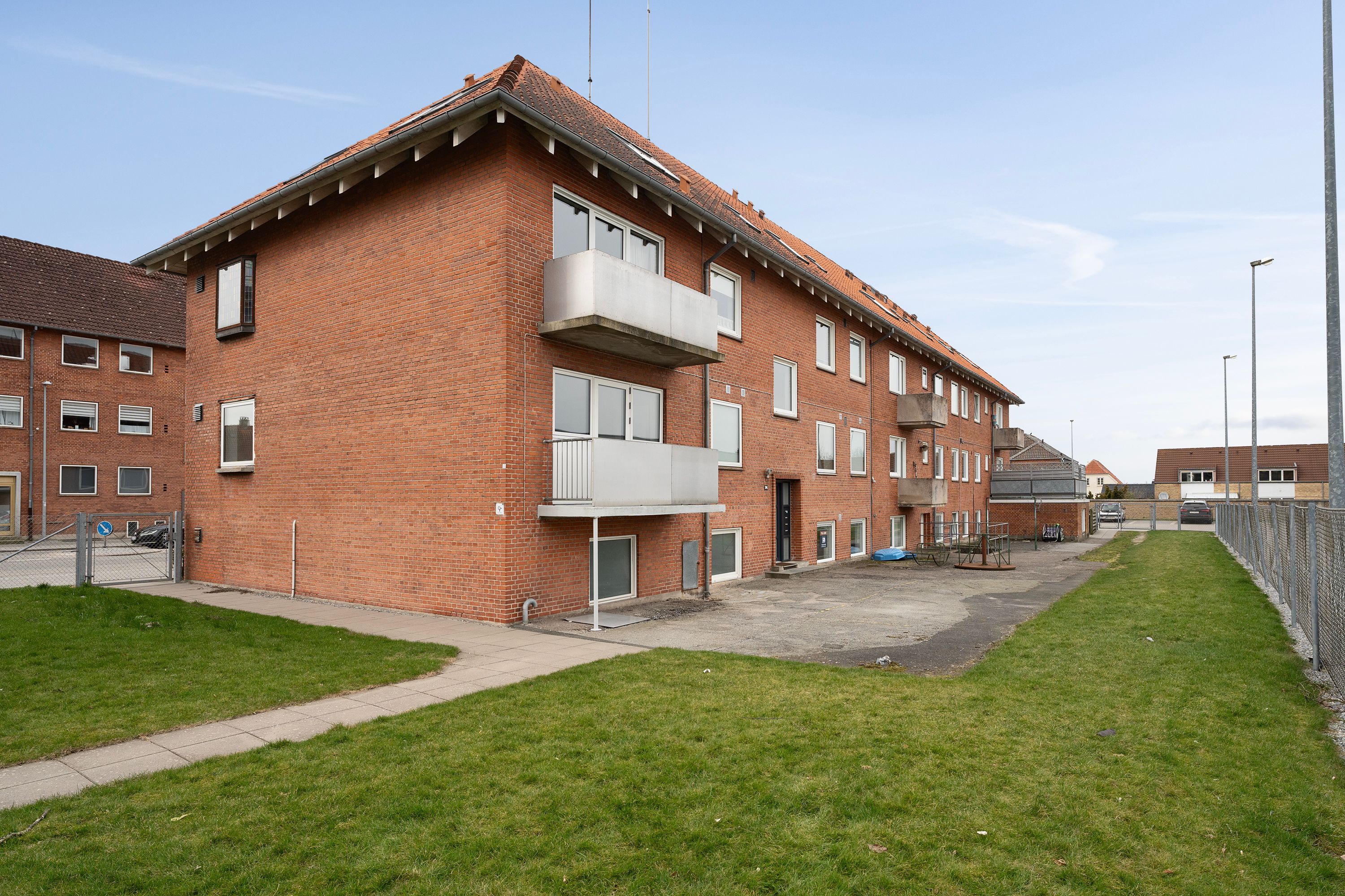 En stor rødmaurstensbygning med garageport og parkeringsplads, smukt grønne græspladser og en række høje søjler med