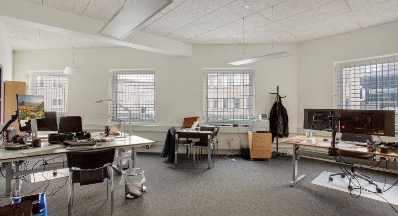 Kontor med skrivebord, stole, computere, monitorer, højtalere, kaffemaskine, papkasser og skraldespand i et moderne,