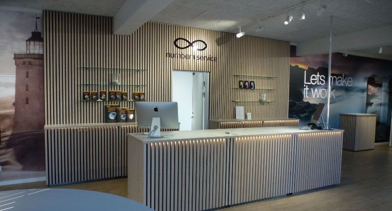 En kontorfællesskab med en stor skrivebord, en monitor og et køkken med en stor, slank væg og hylder med produkter