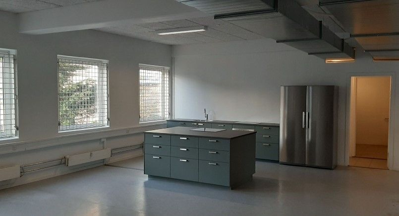 Rummelig stue med åbent køkken og store vinduer samt en køleskab og vask i lysegrå og hvid farve