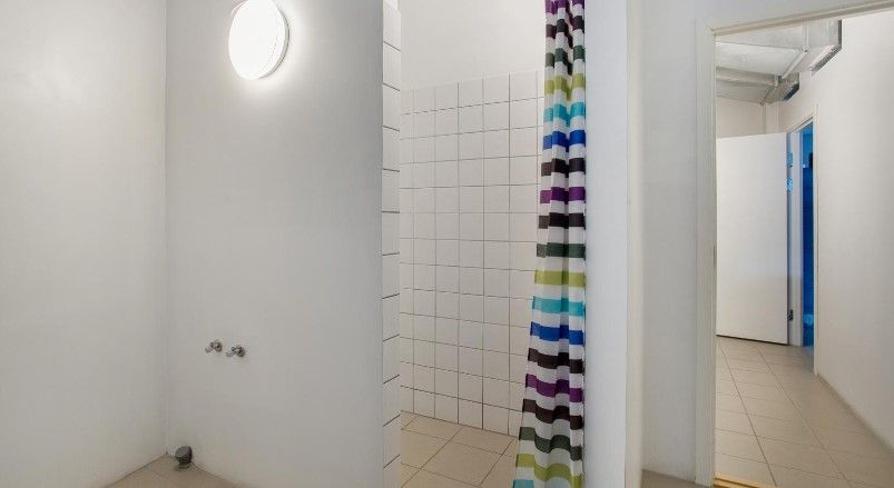 Hvidt og pænt badeværelse med hvidt keramikloft og hvide flisede vægge, farverige brusegardin og åbent kabinet med hvide døre