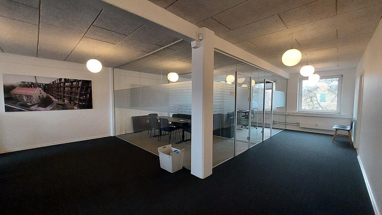 En nyistandsat kontorlokation med bord, stole og glasvægge i et lyst rum med klædt gulv og hængelampe.