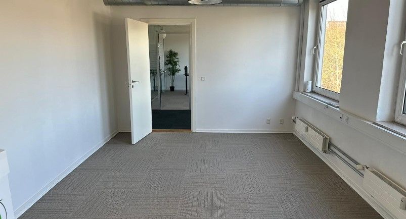 Lyst og rummeligt lejemål med højloftede værelser og moderne gulvbelægning. Vinduet giver lys og udsigt til træer. Døren er